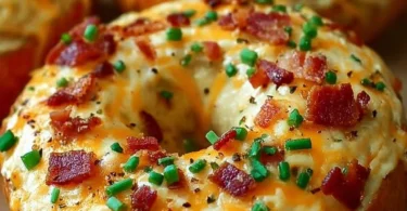 Creamy bacon cheddar bagels stacked on a plate, garnished with herbs.