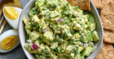 Herby avocado egg salad in a bowl, garnished with fresh herbs.