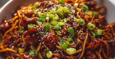 Plate of sticky garlic chicken noodles garnished with green onions