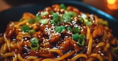 Delicious sticky garlic chicken noodles served in a bowl garnished with green onions.